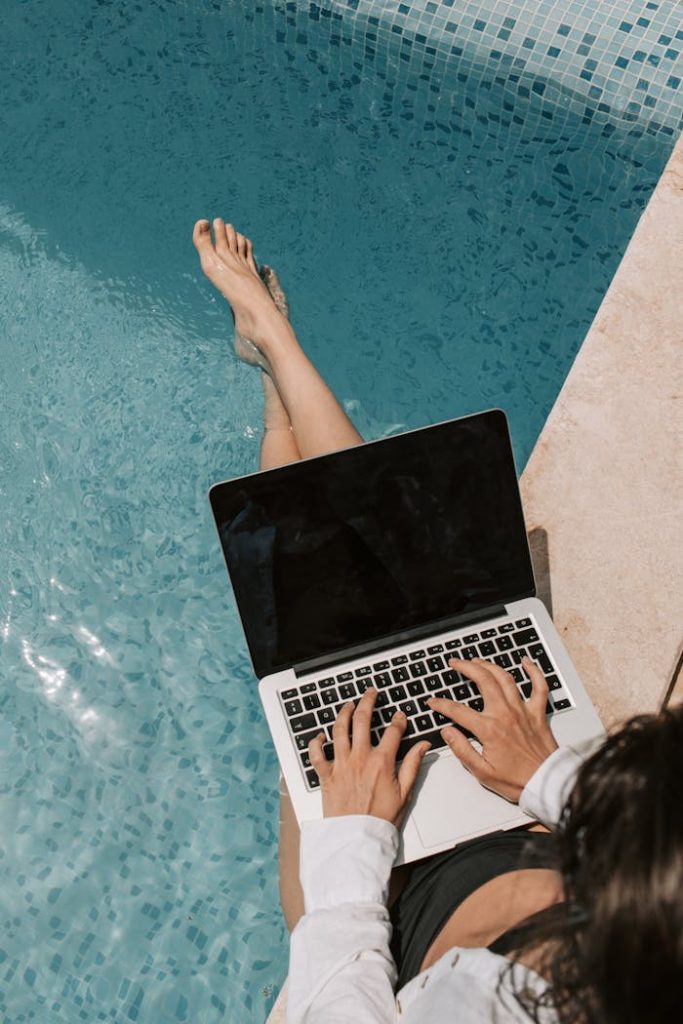 pexels-photo-7903138 Woman working remotely on a laptop by the poolside, enjoying summer outdoors.